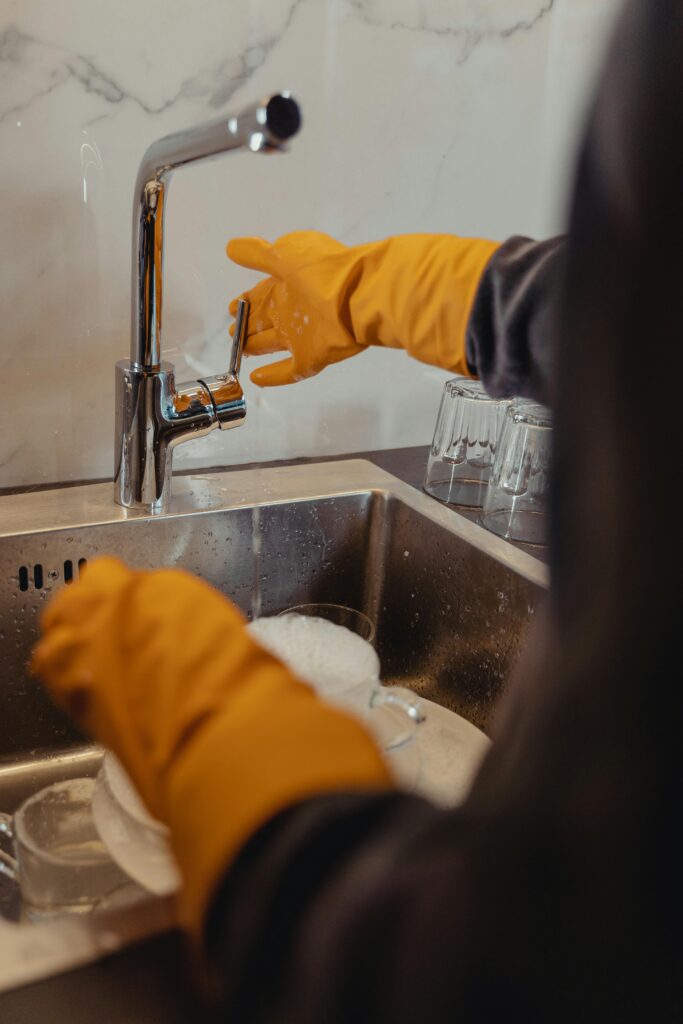 Close-up of a person washing dishes with yellow gloves in a kitchen sink.