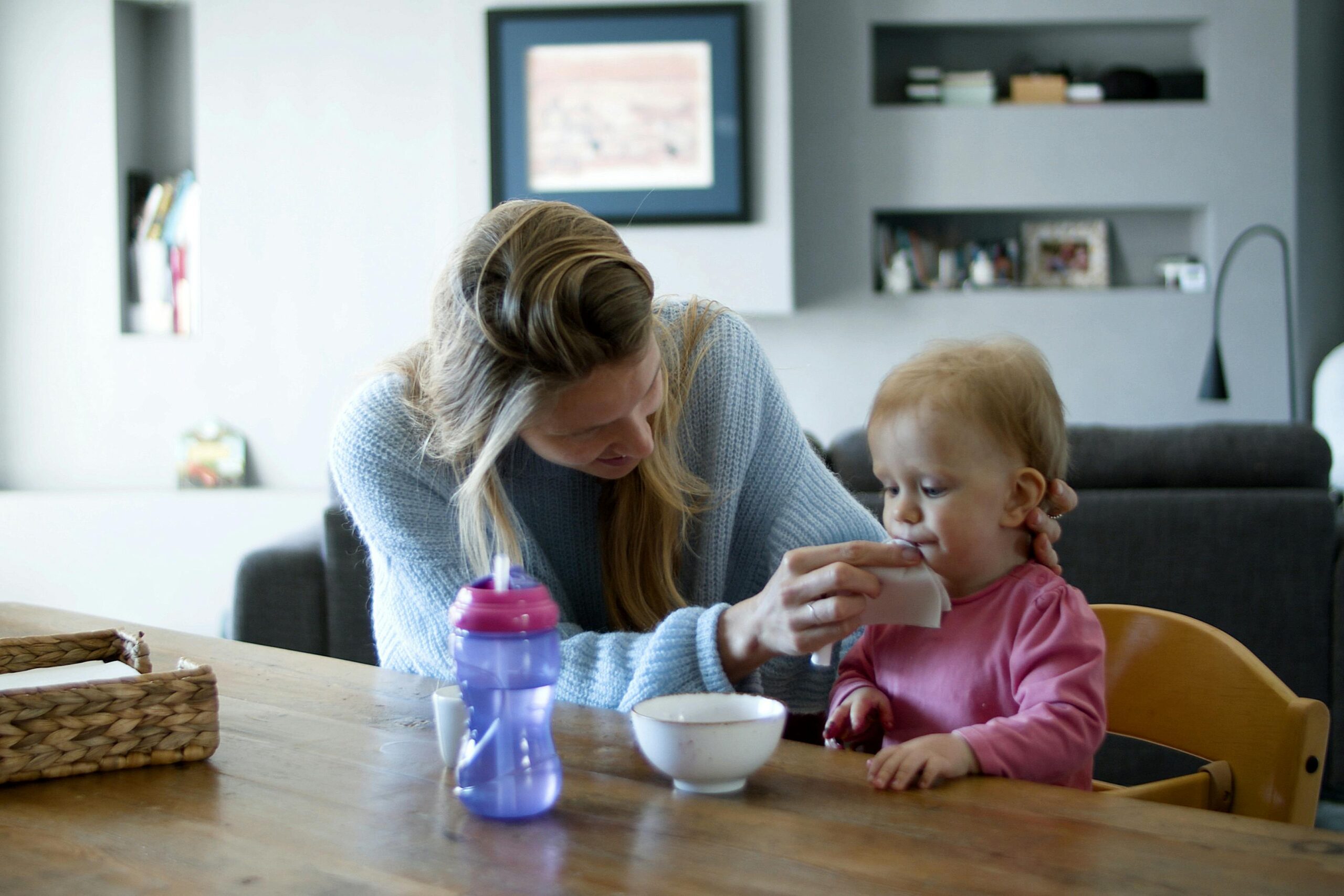 A nurturing woman cleans her baby's face at a kitchen table, showcasing domestic care and bonding.